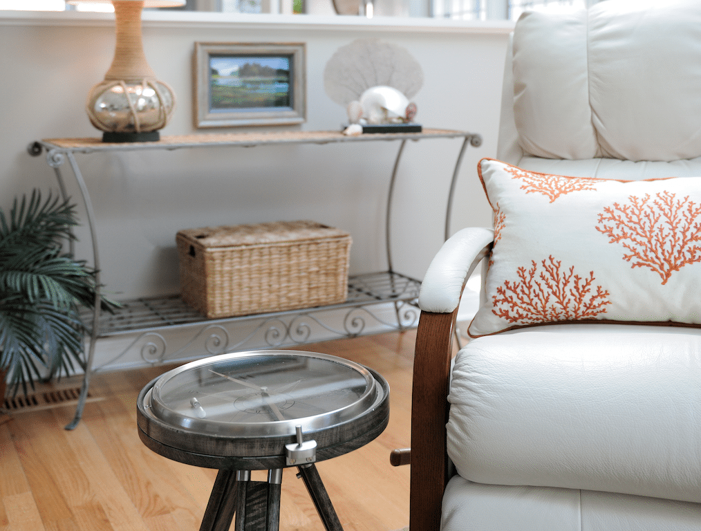 Round gray metal framed clear glass-top end table beside white fabric recliner